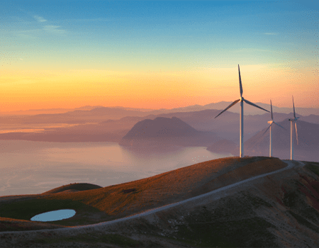 Wind turbines on a hill overlooking a body of water at sunset.