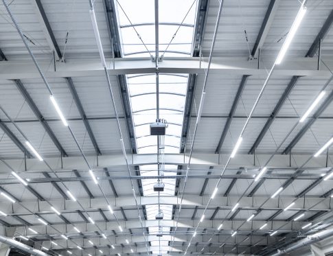 Interior of an industrial warehouse with metal trusses and fluorescent lights.