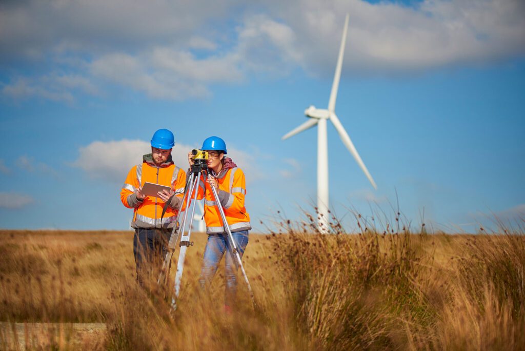 Two engineers in safety gear conducting a survey near a wind turbine.