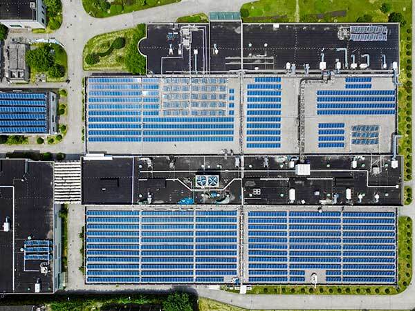 Aerial view of a large industrial building with extensive blue solar panels on the roof.