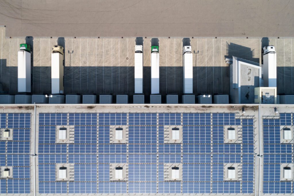 Aerial view of a rooftop covered with solar panels adjacent to parked delivery trucks.