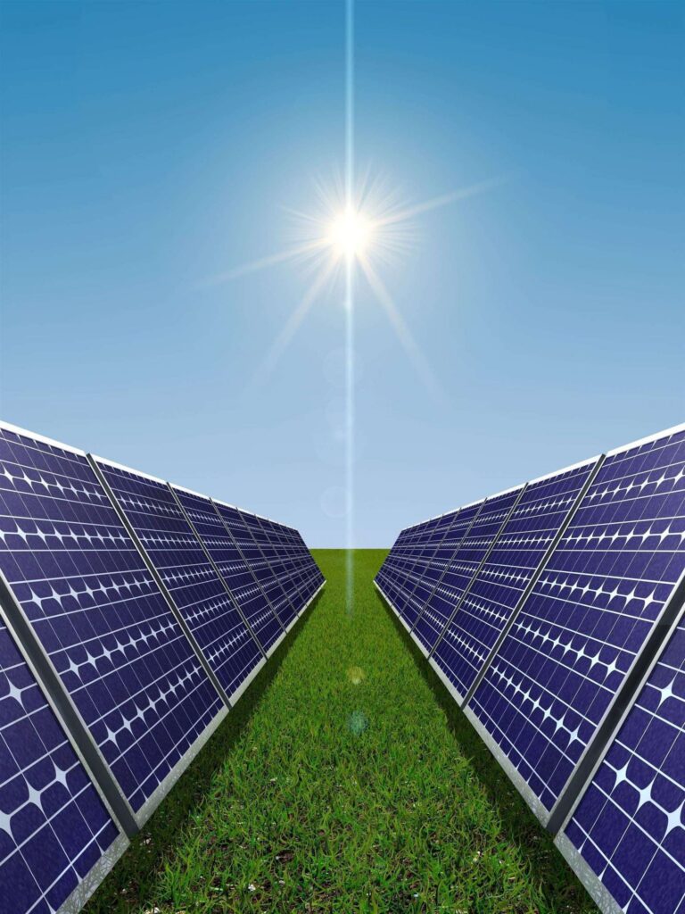 Solar panels arranged in rows on a green field under a clear blue sky with the sun shining brightly.