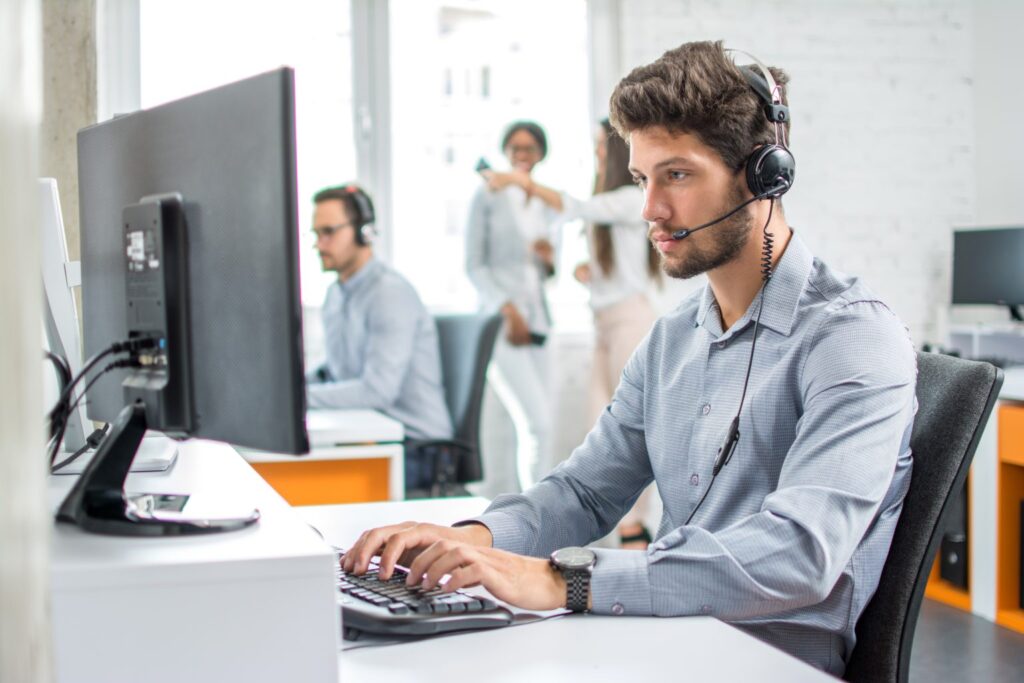 A customer service representative with a headset working at a computer in an office setting.